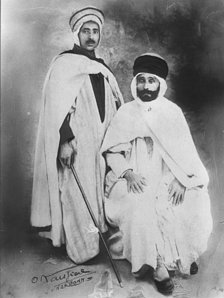 1920. Mon père, Brahim, debout, légèrement de coté et son père Saïd assis sur une chaise, personnages magnifiques dans leurs somptueux habits traditionnels.