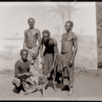 Photo de propagande coloniale. Des hommes congolais font une démonstration de travail du métal devant un décor peint. Exposition universelle Anvers, 1894.© Collection MAS.