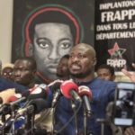 Un portrait d’Omar Blondin Diop est affiché derrière le militant sénégalais Guy Marius Sagna au siège du Front pour une révolution anti-impérialiste populaire et panafricaine (Frapp), à Dakar, le 25 mars 2021. SEYLLOU / AFP